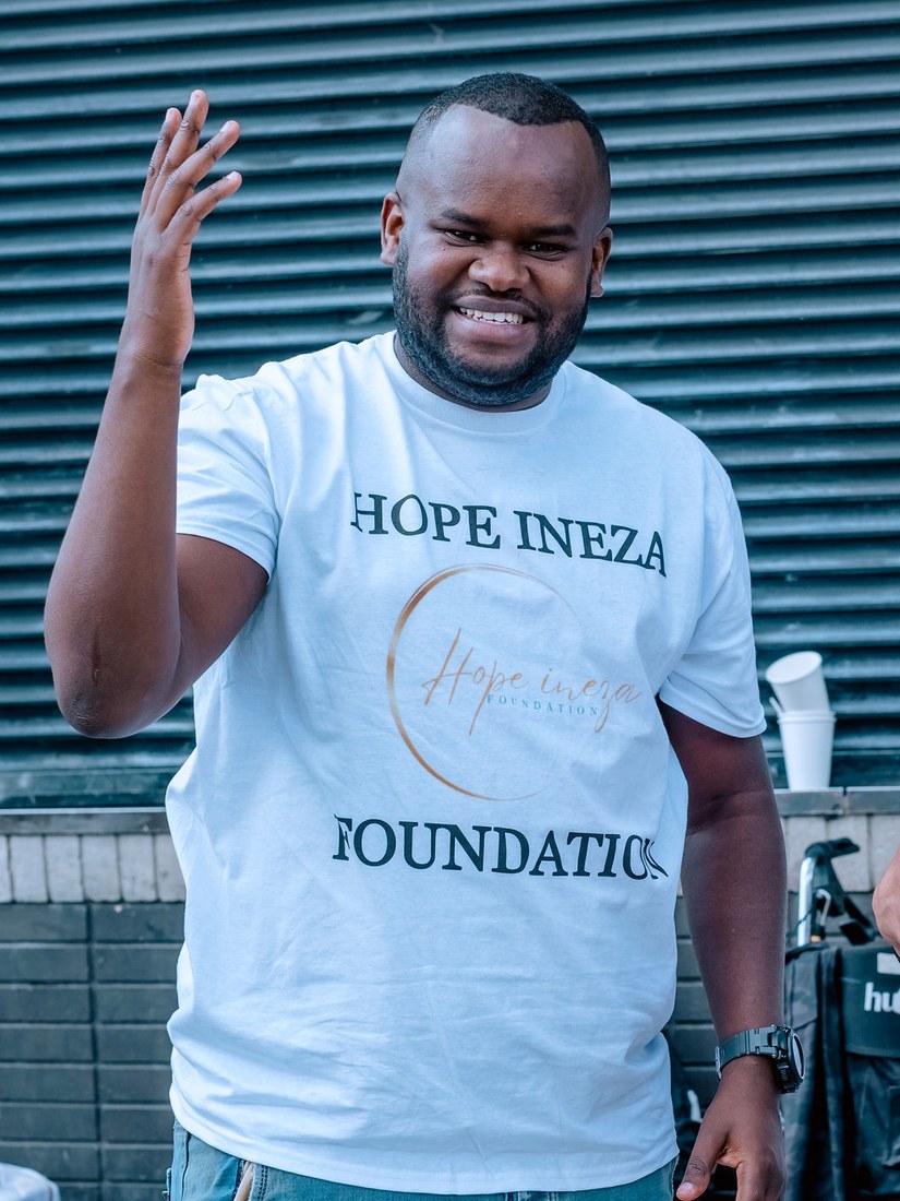 A Hope Ineza Foundation team member in a branded shirt greeting people during a street outreach