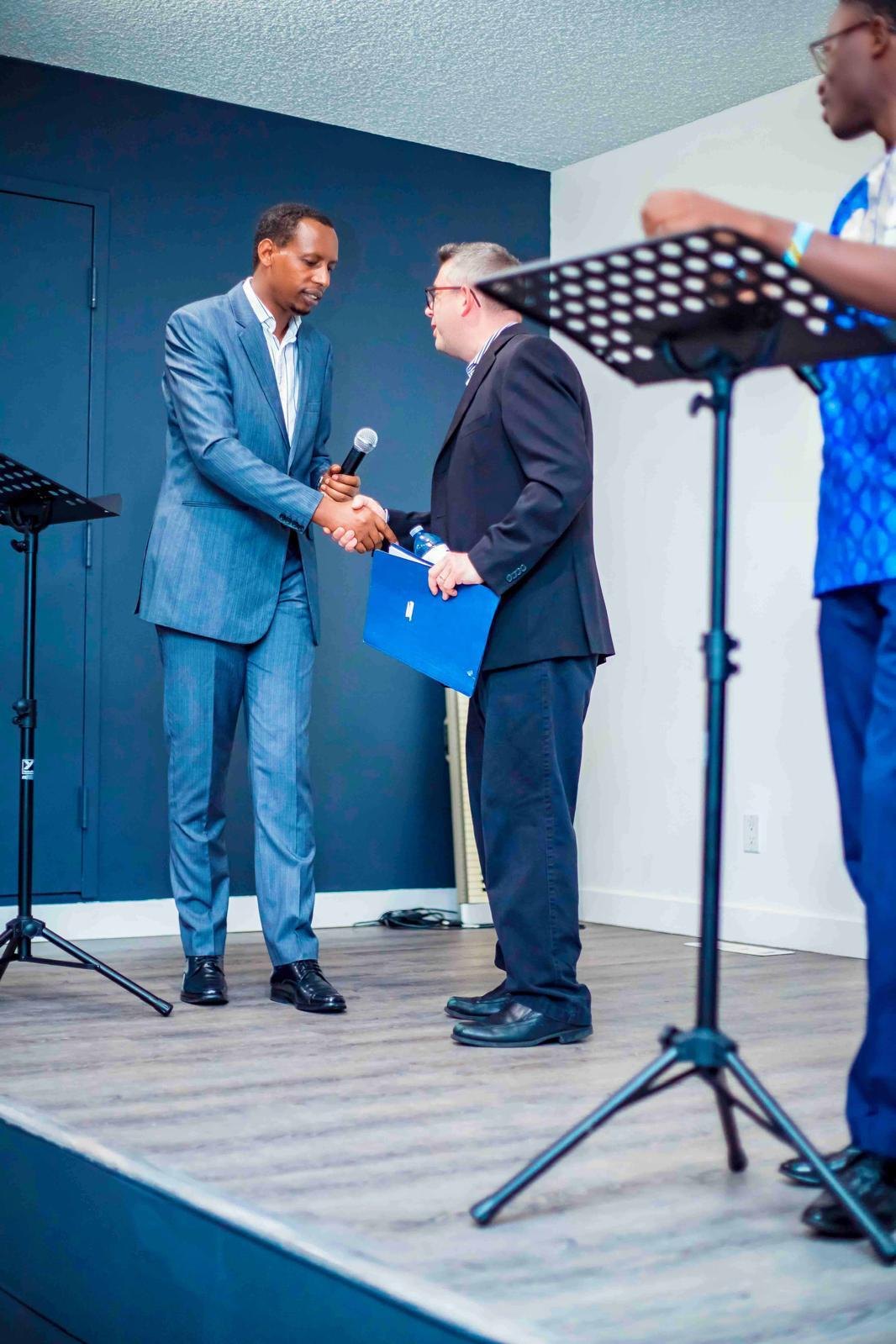 Rev. Pastor Jean Paul Mutabazi shaking hands with a partner on stage